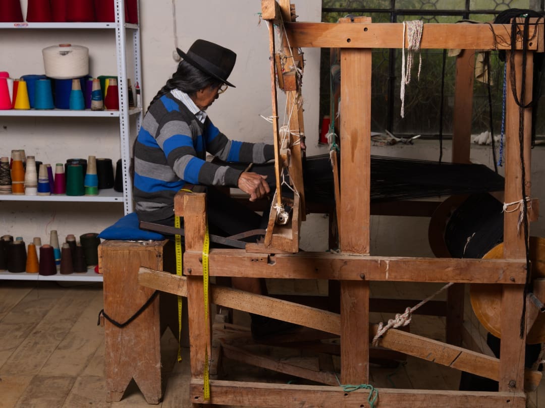 Tejiendo Telas Tradicionales Un Saraguro con sombrero tejiendo telas tradicionales.