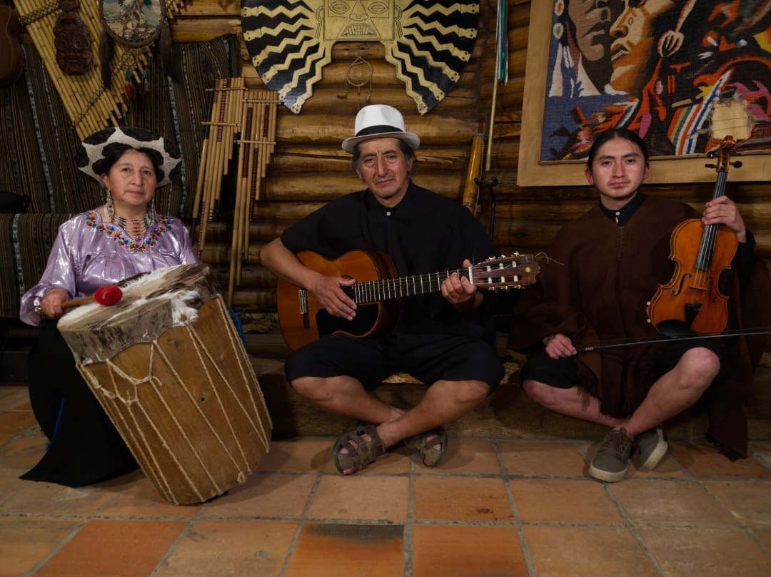 Andean music Three musicians with traditional instruments, dressed in the typical Saraguro dress, sitting on the floor.