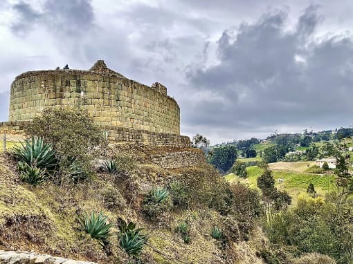 Templo del Sol de Ingapirca Templo del Sol de Ingapirca, resplandeciendo en un tono dorado bajo el sol, con un cielo nublado como fondo.