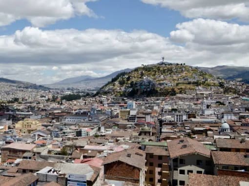 Centro Histórico de Quito Vista de los tejados del Centro Histórico de Quito desde la Basílica del Voto Nacional, con el Panecillo difuminado en el fondo bajo un cielo parcialmente nublado.