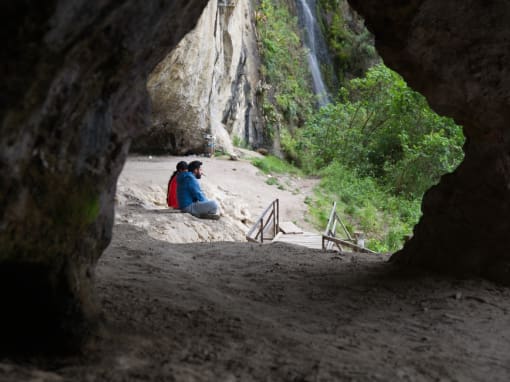 Baños del Inca Two people sitting on the edge of a cave with the Baños del Inca waterfall in the background.