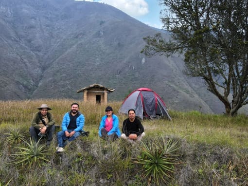 Four happy campers pose for a photo in front of their tent with a spectacular view of the surrounding Andean landscape.