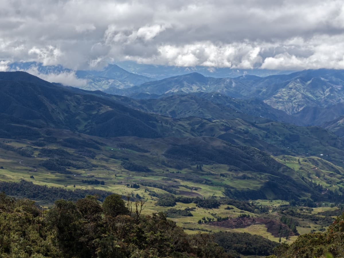 Landscapes of Saraguro View of farmland in the foreground, with the majestic Andes mountain ranges in the background, under a partly cloudy sky.