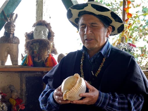 Taita Luis with closed eyes holds a conch shell while guiding a sacred ritual.