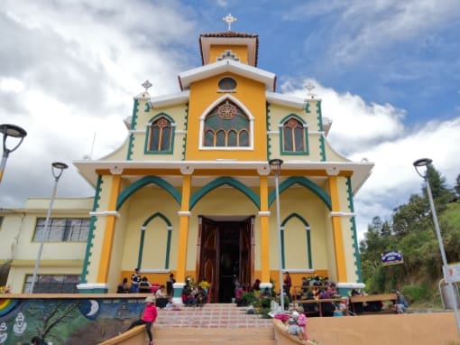 Iglesia de San Lucas La Iglesia de San Lucas, pintada en tonos amarillos con detalles en azul y verde, con niños jugando en las escalinatas y mujeres frente al templo preparando un festival.
