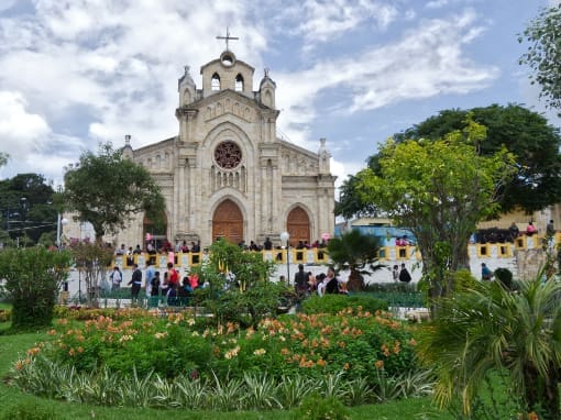 The imposing church of Saraguro seen through a garden in the park on a partly cloudy day.