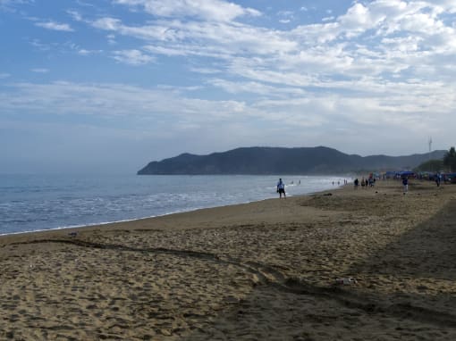Puerto Lopez Mañana en la playa de Puerto López con personas a lo lejos, cielo azul con nubes ligeras y mar tranquilo con pequeñas olas.